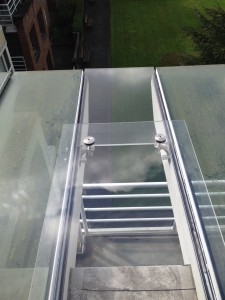 Glass canopy system with custom glass holder hardware for residential apartment exterior skylight.